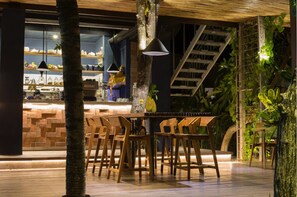 Um espaço de refeições interno com cadeiras de madeira e uma mesa, rodeado por estantes com utensílios de cozinha e uma escada.