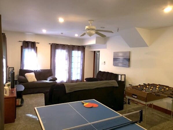 A living room with a ping pong table, sofa, and foosball table.