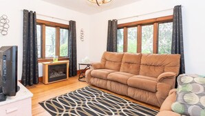 A living room with a sofa, a television, a fireplace, and large windows with curtains. - Spacious Private Home with Large Deck  (South Haven)