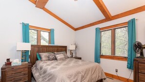 A bedroom with a wooden headboard, a bed with a grey patterned bedspread, two bedside tables with lamps, and a ceiling fan. - Spacious Private Home with Large Deck  (South Haven)