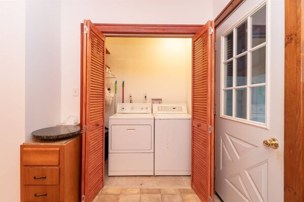 A laundry area with two white washers and dryers, a wooden cabinet with drawers, and a door with a window. - Spacious Private Home with Large Deck (South Haven)