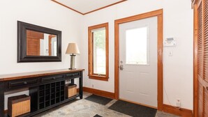 A hallway with a stone floor, a wooden console table with drawers, a mirror, a lamp, and two doors with windows. - Spacious Private Home with Large Deck  (South Haven)