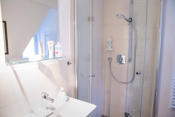 A modern bathroom with a glass shower enclosure, a white sink, and toiletries on a shelf.