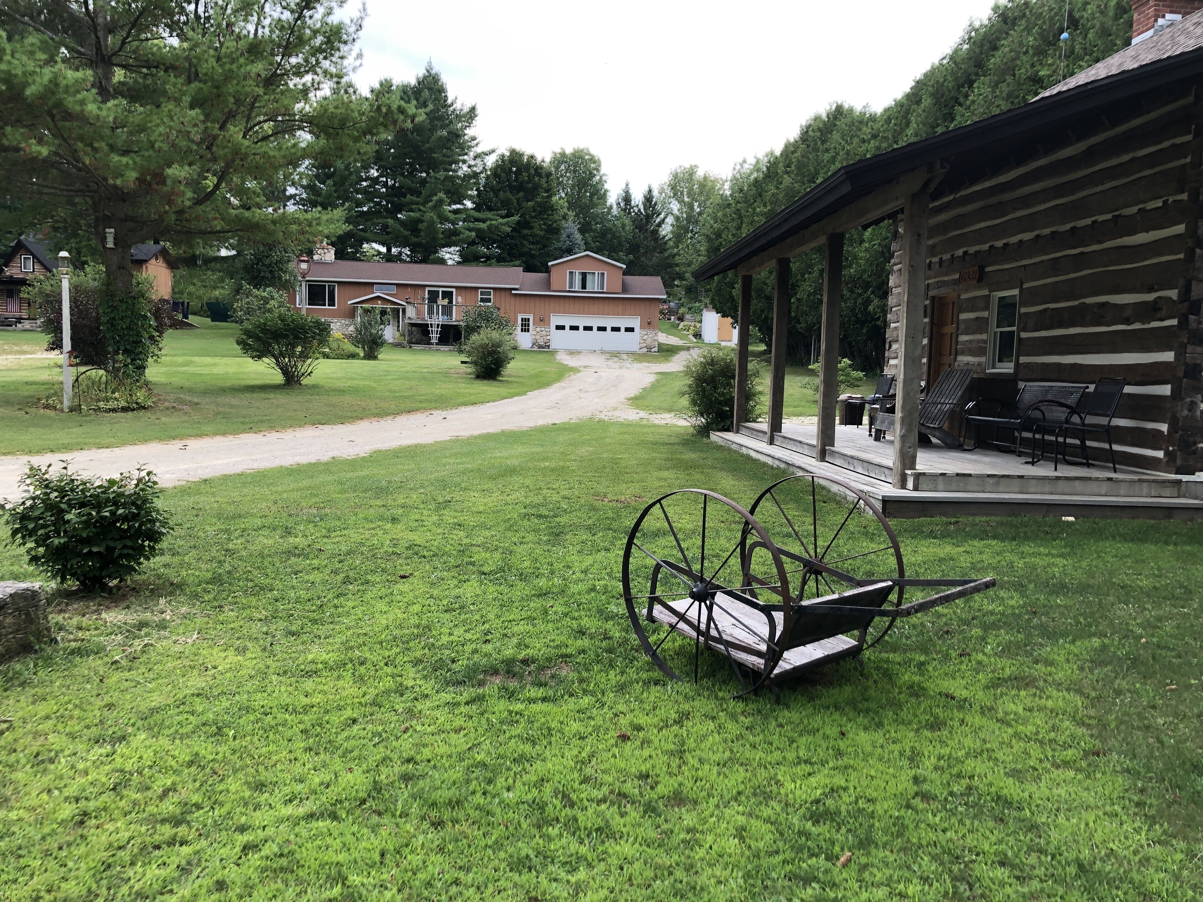 Eine Rasenfläche mit einer Schaukel, einer überdachten Terrasse mit Bänken und einem Gebäude mit Garage im Hintergrund.