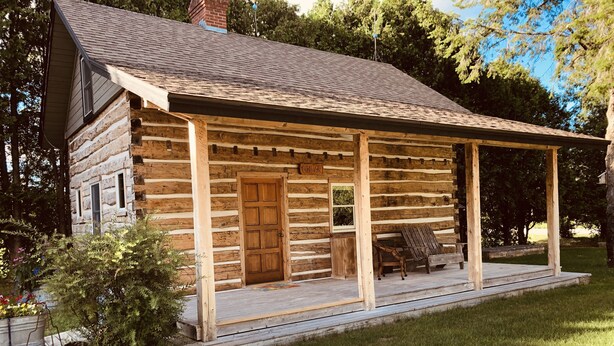 Une cabane en rondins avec un porche, une porte en bois et un banc.