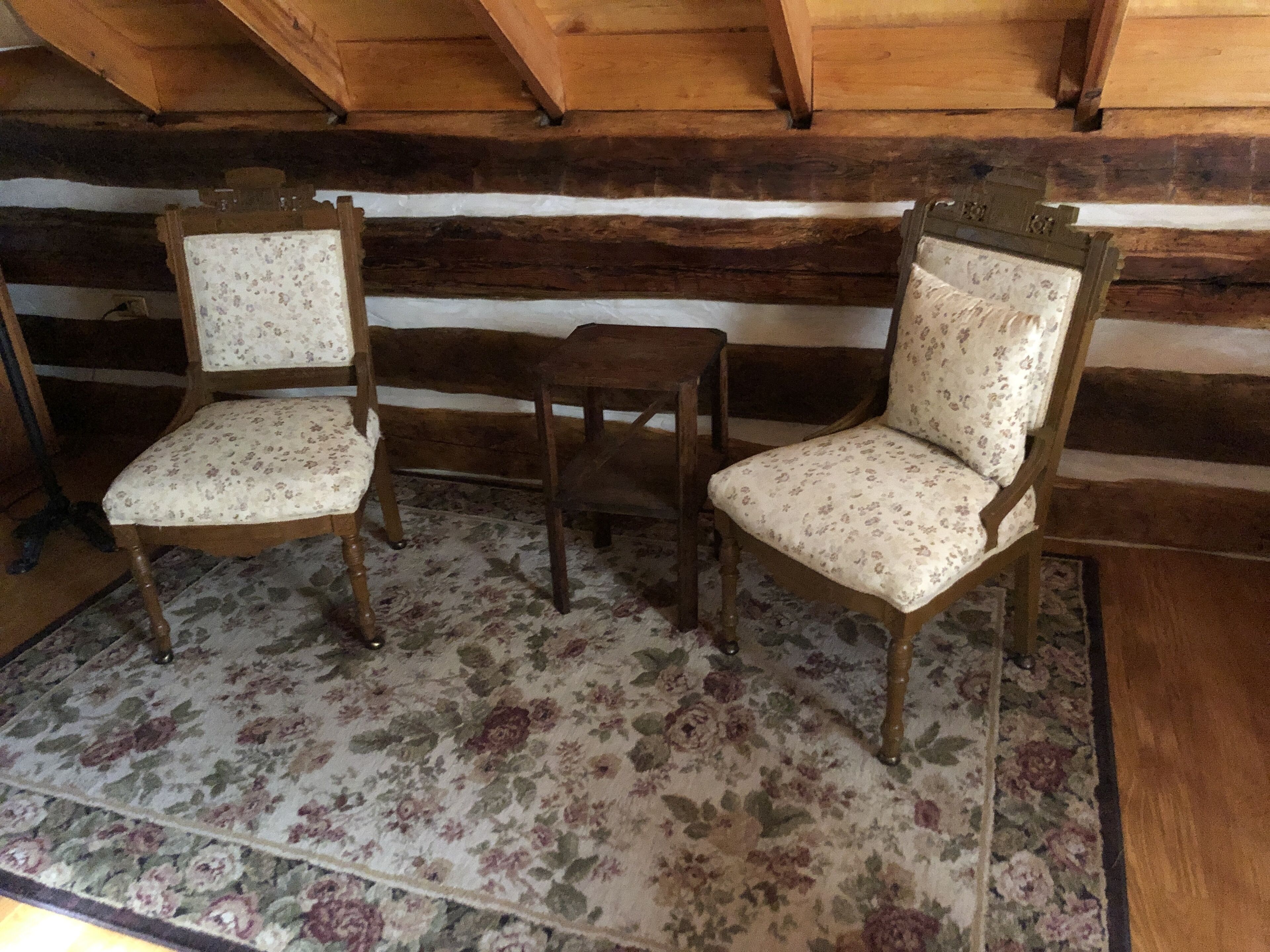 A rustic wooden cabin interior with two wooden chairs with floral upholstery and a small wooden table.