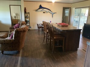 Een eetgedeelte met een houten tafel en stoelen, een muurschildering van vissen, en een keuken met een koelkast en een spoelbak.