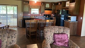 A kitchen with wooden cabinets, a refrigerator, a microwave, and a dining area with patterned chairs and a table. - Aggie Game day in the country outside of College Station!  (Cameron)