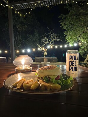 A meal with a sandwich, fries, and a drink on a table under string lights. - Bosque de Aventura & Glamping El Refugio  (La Mesa)