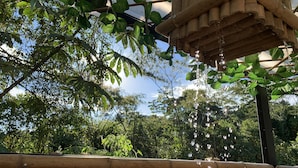 Una struttura in legno con foglie pendenti e gocce d'acqua, immersa nel verde lussureggiante.