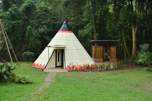 A conical tent with a door, surrounded by a garden with red flowers and a small wooden structure. - Bosque de Aventura & Glamping El Refugio  (La Mesa)
