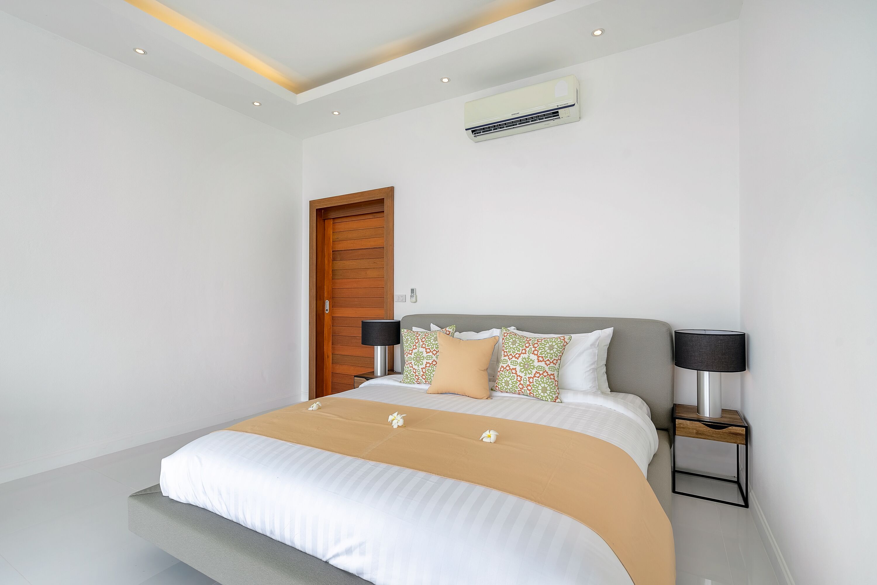 A modern bedroom with a large bed, a wooden door, and two bedside tables with lamps.