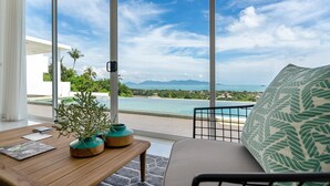 Sala de estar moderna com uma grande porta de vidro que dá para uma varanda com vista para uma piscina e o oceano.