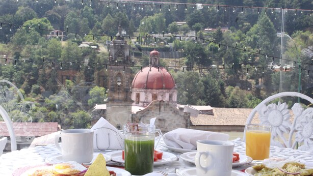 A table set with breakfast items including a plate of eggs, a green drink, and orange juice, with a scenic view of a dome and trees in the background.