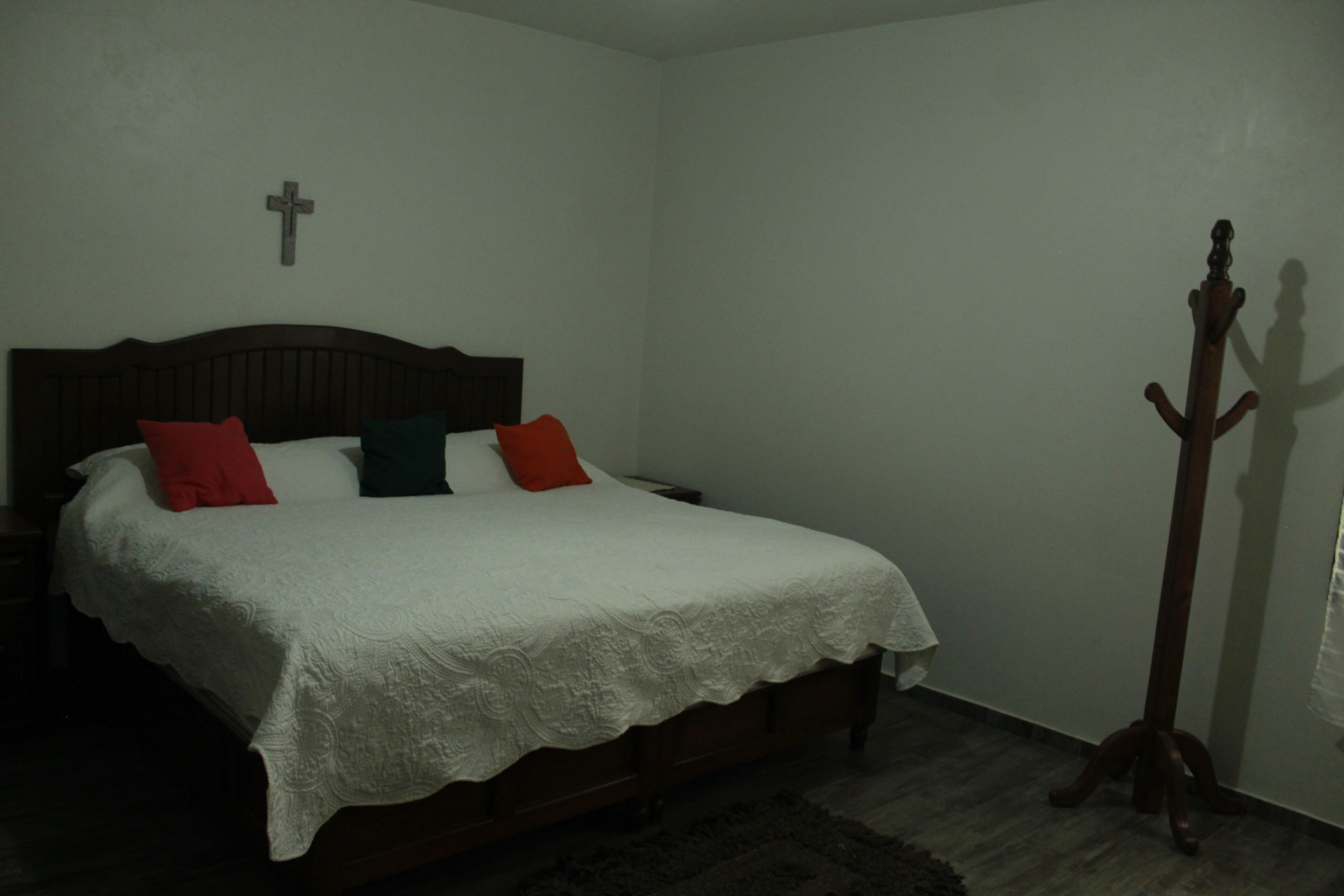Un dormitorio con una cama de madera, ropa de cama blanca y un perchero de madera.