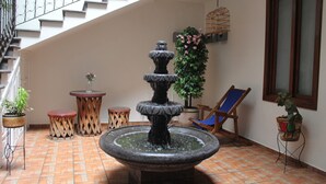 A multi-tiered fountain in a courtyard with tiled flooring, potted plants, a wooden chair, and a staircase.