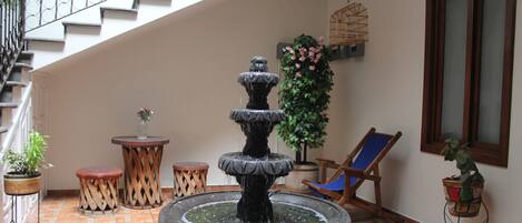 Een meerlaags fontein in een binnentuin met betegelde vloer, potplanten, een houten stoel en een trap.