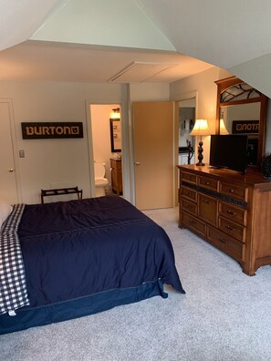 A bedroom with a large bed, a dresser, a mirror, and a door leading to a bathroom.