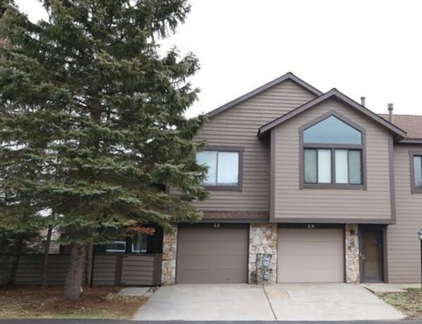 A two-story house with a garage, a large tree in front, and a stone facade.