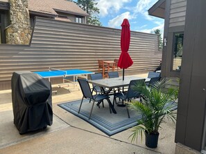 An outdoor patio with a table and chairs, a red umbrella, and a covered grill.