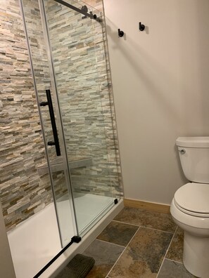 A bathroom with a glass-enclosed shower, a white toilet, and stone-patterned walls.