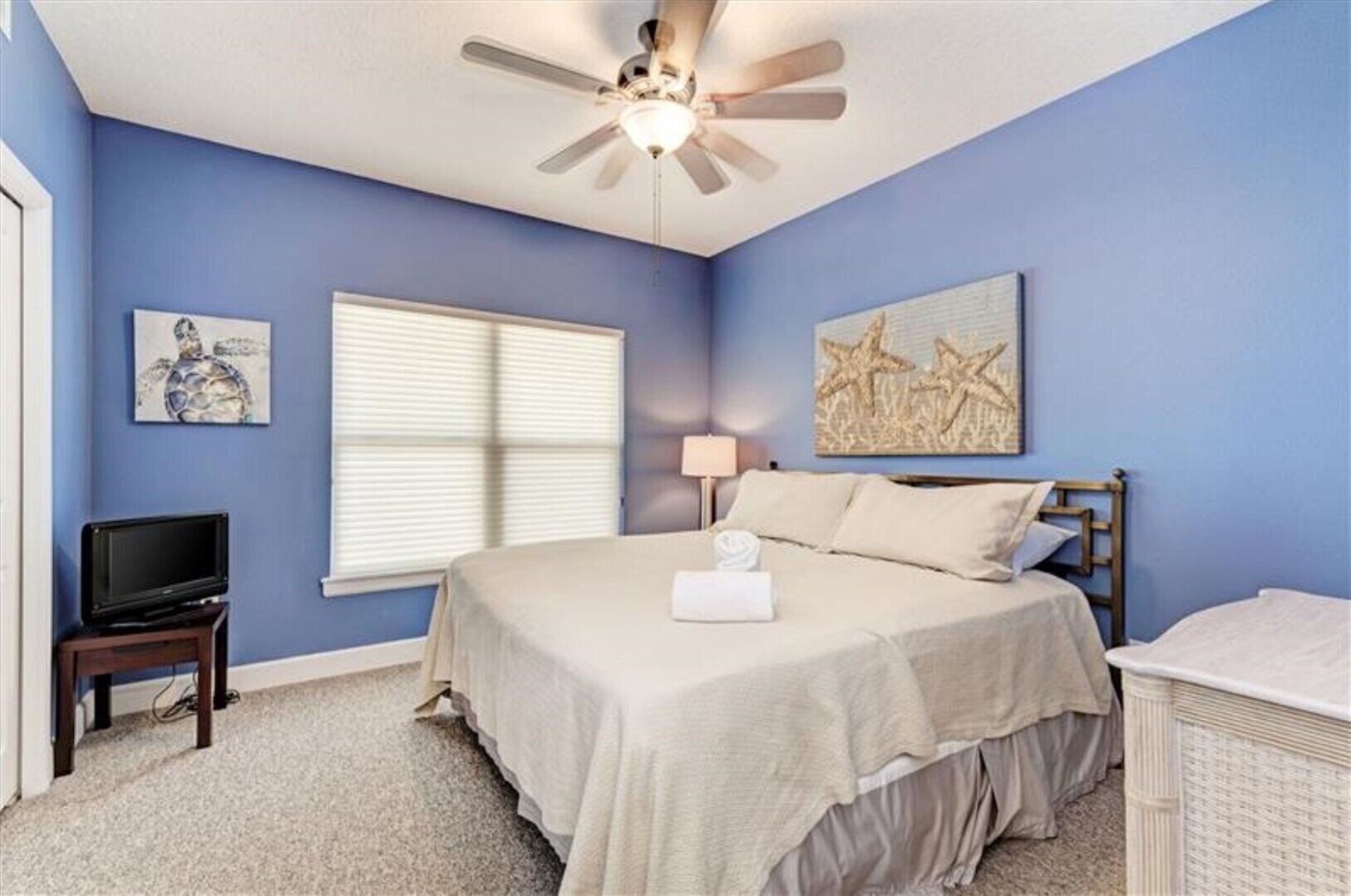 A bedroom with a bed, a ceiling fan, a television, and artwork on the walls.