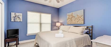 A bedroom with a bed, a ceiling fan, a television, and artwork on the walls.