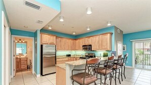 A kitchen with wooden cabinets, a stainless steel refrigerator, a microwave, and a bar area with stools. - The Sea Grape, end unit, walk to beach (Bradenton Beach)