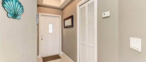 A hallway with a white door, a white closet with louvered doors, a small decorative shell on the wall, and a recessed ceiling light.