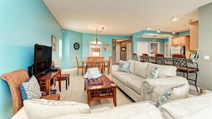 A living room with a TV, sofa, coffee table, and dining area with chairs and a table. - The Sea Grape, end unit, walk to beach (Bradenton Beach)