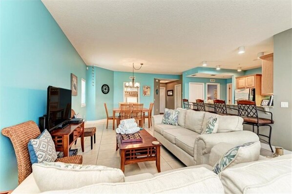 A living room with a TV, sofa, coffee table, and dining area with chairs and a table.