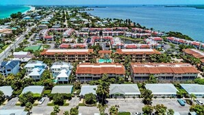 An aerial view of a coastal resort with multiple buildings, a beach, and a clear view of the ocean. - The Sea Grape, end unit, walk to beach (Bradenton Beach)