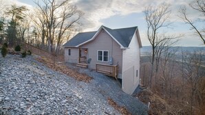 A single-story house with a sloped roof, a front porch, and a gravel driveway. -  Large-Group Cabin near Luray · Sleeps 12 · Hot Tub & Mountain Views (Rileyville)