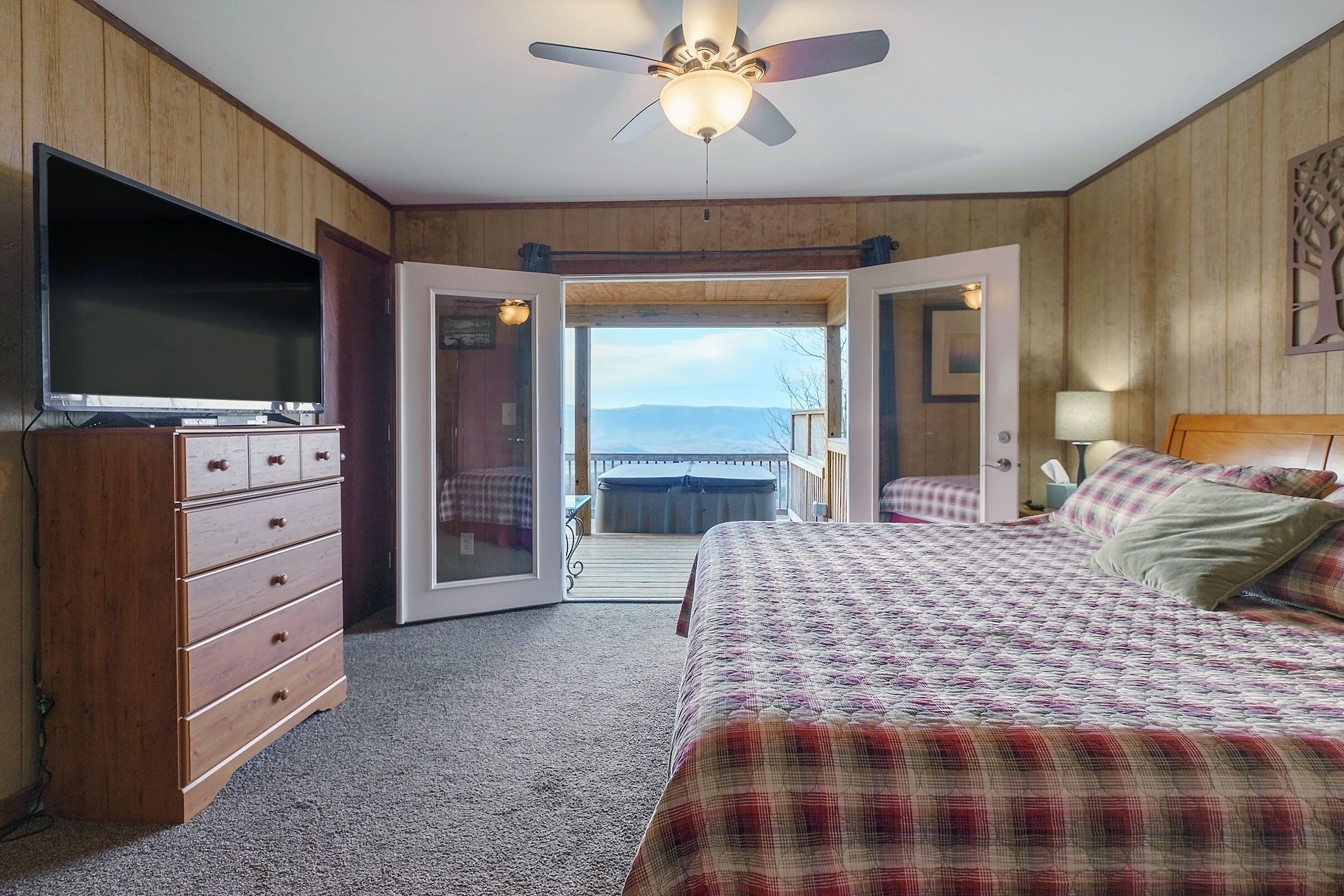 Un dormitorio con cama, cómoda, televisor y puerta que da a un balcón con vistas.