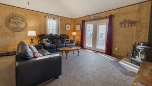 A cozy living room with a leather sofa, a wooden coffee table, and a fireplace. -  Large-Group Cabin near Luray · Sleeps 12 · Hot Tub & Mountain Views (Rileyville)
