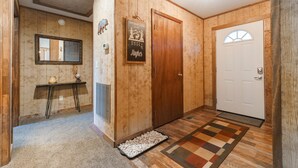 A wooden-paneled hallway with a mirror, a welcome sign, a door, and a patterned rug. -  Large-Group Cabin near Luray · Sleeps 12 · Hot Tub & Mountain Views (Rileyville)