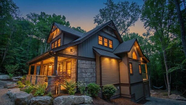 A log cabin with a stone foundation, wooden exterior, and a porch with a stone railing.