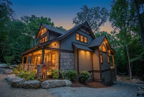 A log cabin with a stone foundation, wooden exterior, and a porch with a stone railing.