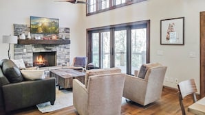 A spacious living room with a stone fireplace, comfortable seating, and large windows offering natural light.