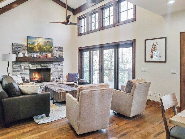 A spacious living room with a stone fireplace, comfortable seating, and large windows offering natural light.