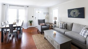 A modern living room with a dining area, a grey sofa, a coffee table, and a chandelier.