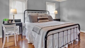 A bedroom with a bed, two bedside tables, a chair, and a chandelier.