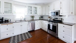 A modern kitchen with white cabinetry, stainless steel appliances, and a wooden floor.