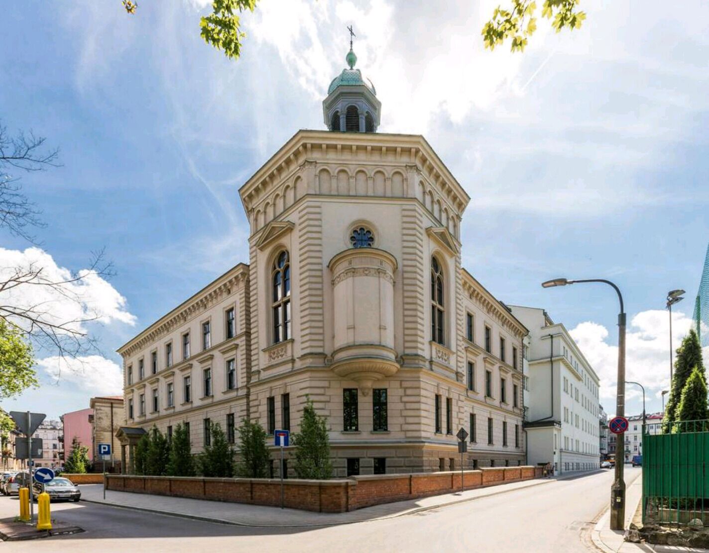 Un grand bâtiment historique, doté d’un dôme imposant et de fenêtres en arc de cercle, situé à l’angle d’une rue, sous un ciel dégagé.