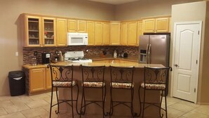 A kitchen with wooden cabinets, a stainless steel refrigerator, a microwave, a stove, and a trash can. - Dove Mountain Retreat - Private pool (Marana)
