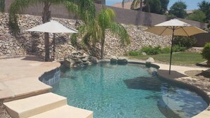 A swimming pool with clear water, stone steps leading into it, and two umbrellas. - Dove Mountain Retreat - Private pool (Marana)