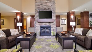 A hotel lobby with two sofas, a fireplace, a flat-screen TV, and a patterned carpet.