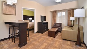 A hotel room with a bed, a desk with a chair, a sofa, a TV, and a lamp.