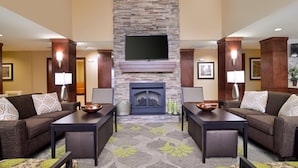 A hotel lobby with two sofas, a fireplace, a flat-screen TV, and a patterned carpet.