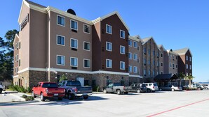 A multi-story hotel with a brown and beige exterior, featuring a stone facade and multiple windows. There are several vehicles parked in front, including trucks and cars.